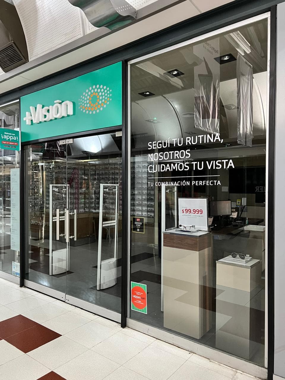 Fachada de óptica +Visión con letrero verde y promociones en su vitrina de cristal.