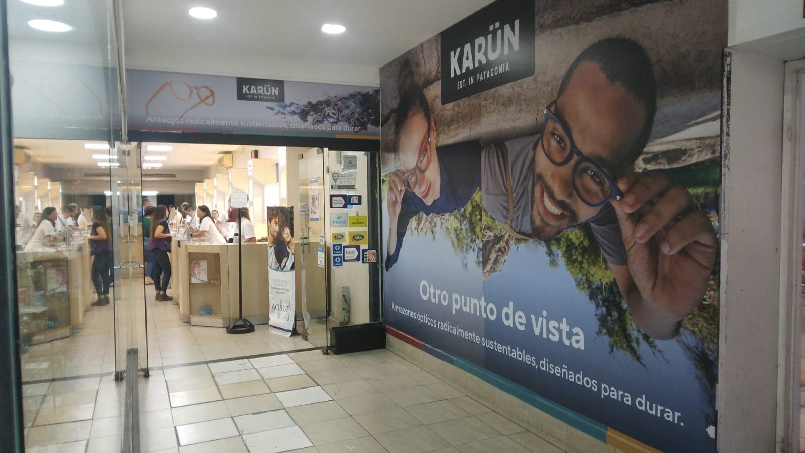 Entrada a una óptica Karün con un gran mural publicitario de personas usando anteojos sustentables.