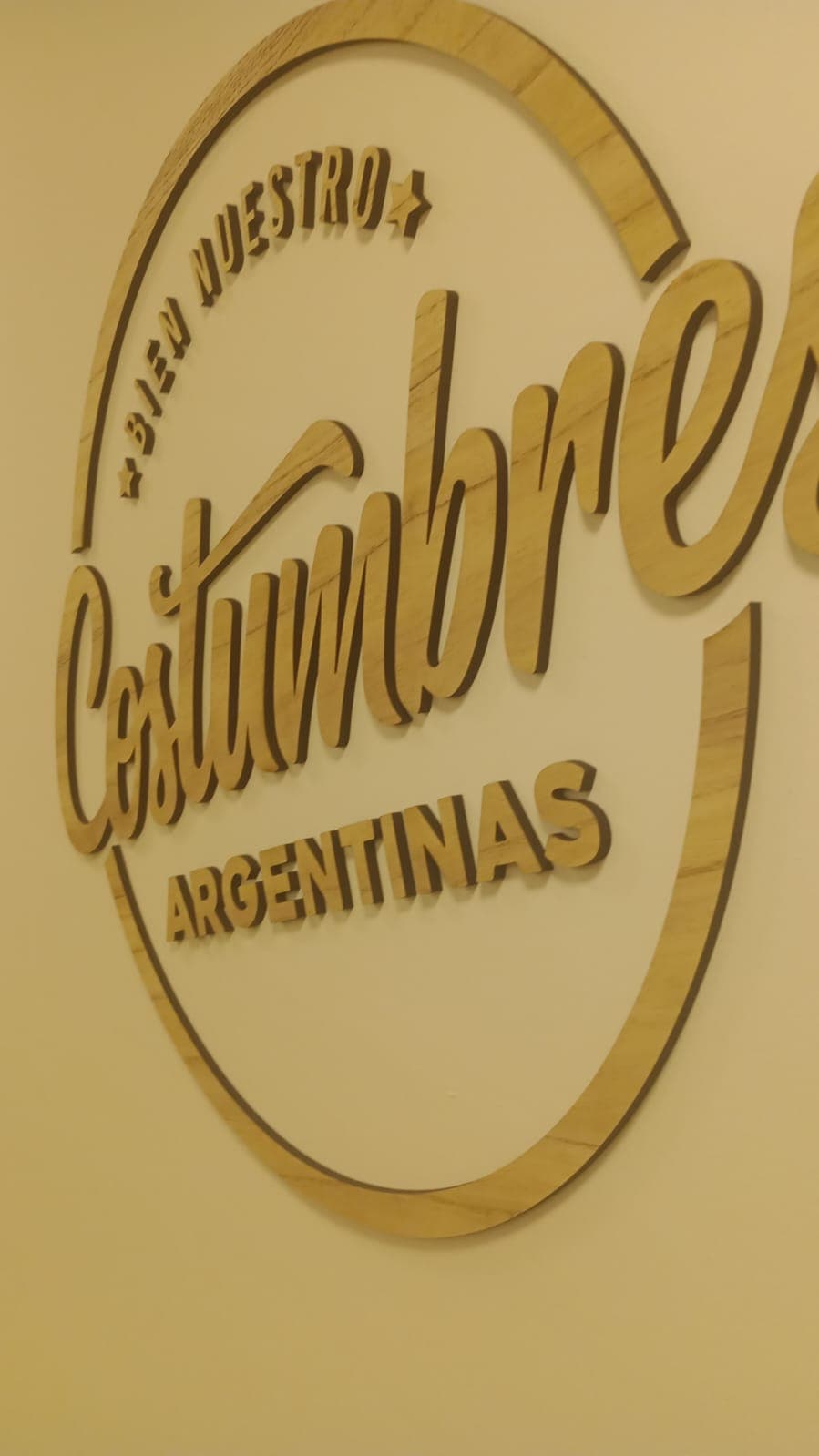 Logotipo circular de madera en relieve con las palabras "Costumbres Argentinas" y "Bien Nuestro".