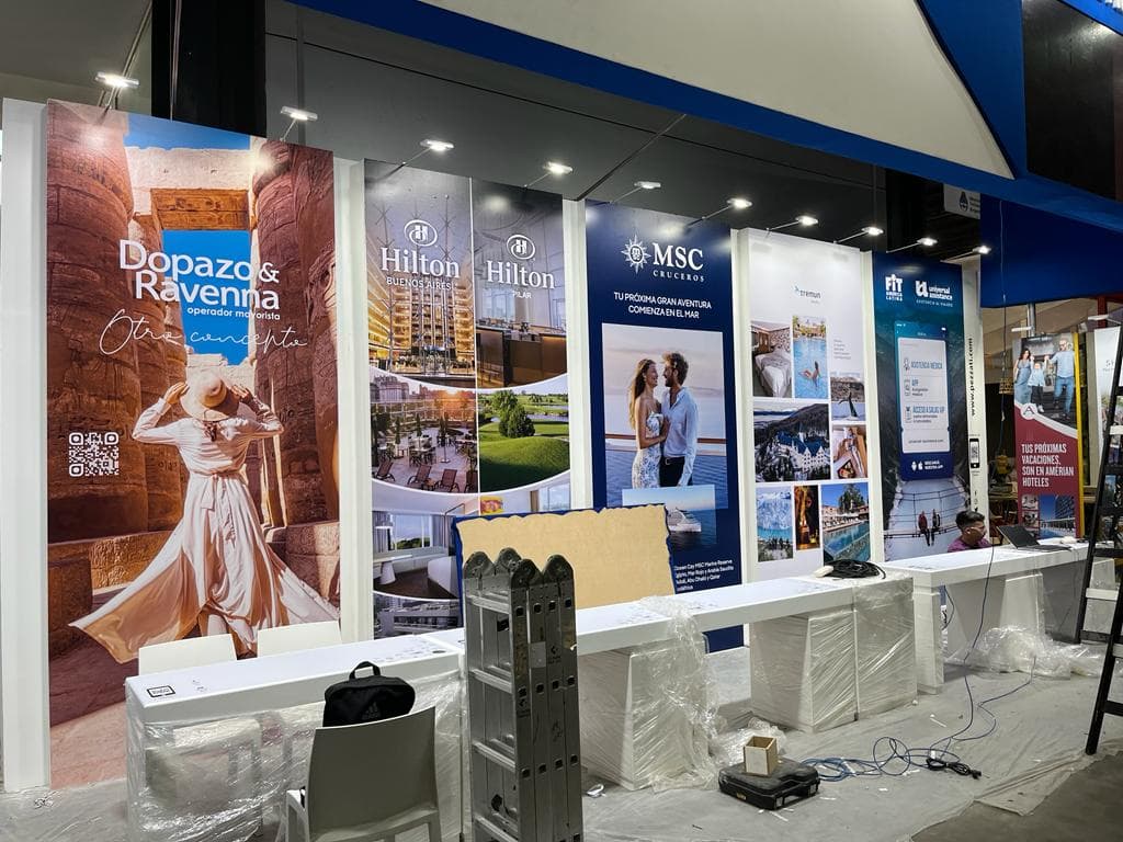 Stand de feria turística con paneles publicitarios de hoteles, cruceros y agencias de viajes.