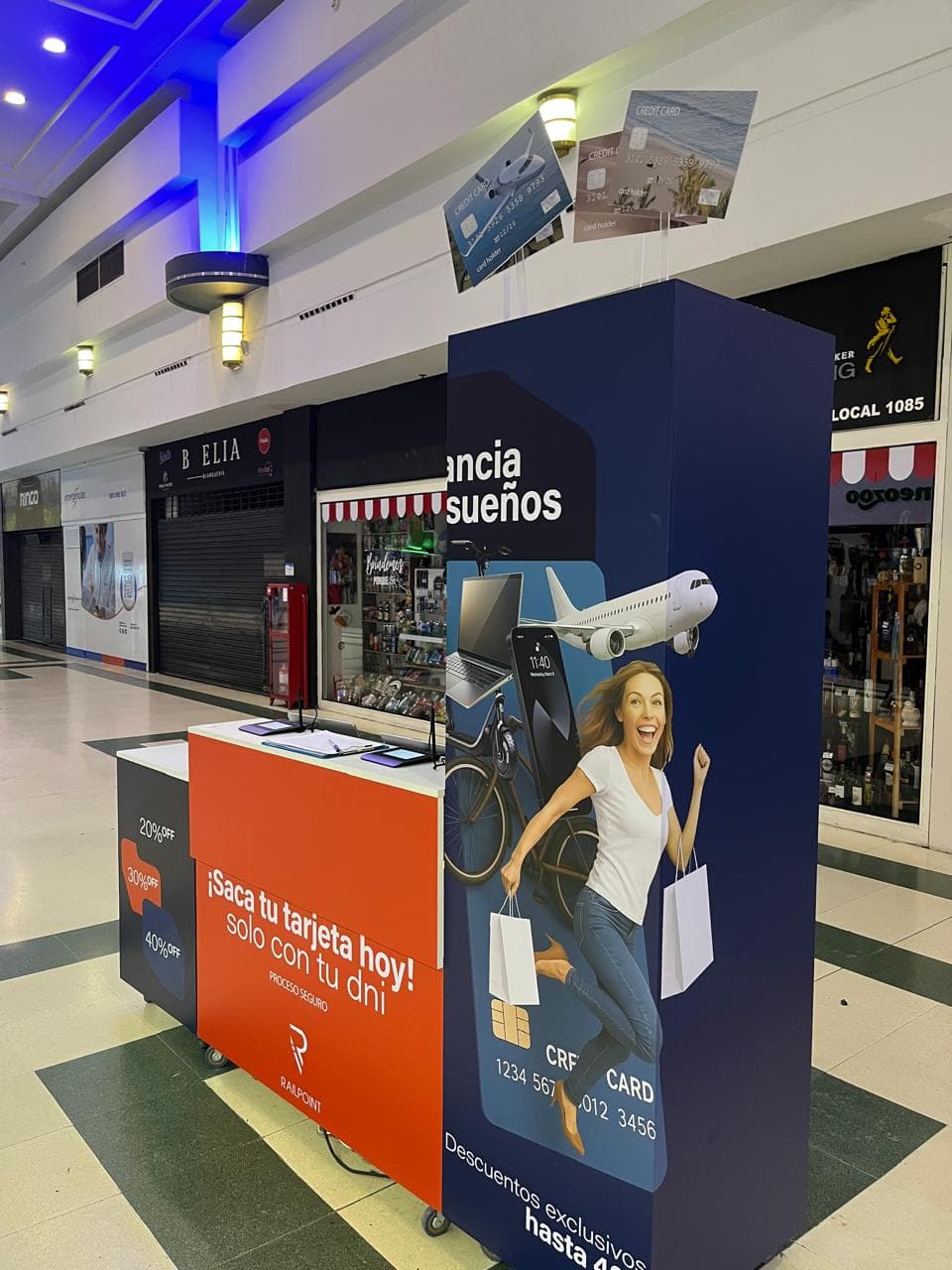 Stand de tarjetas de crédito en un centro comercial con imágenes de viajes y compras.