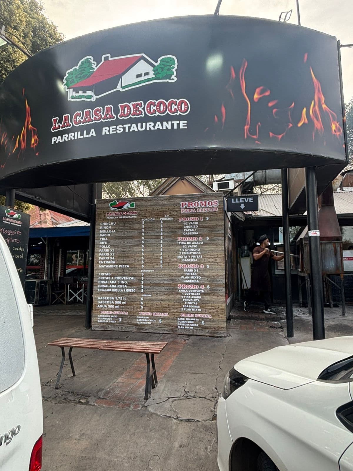 Letrero negro con llamas de La Casa de Coco Parrilla Restaurante sobre un menú detallado.
